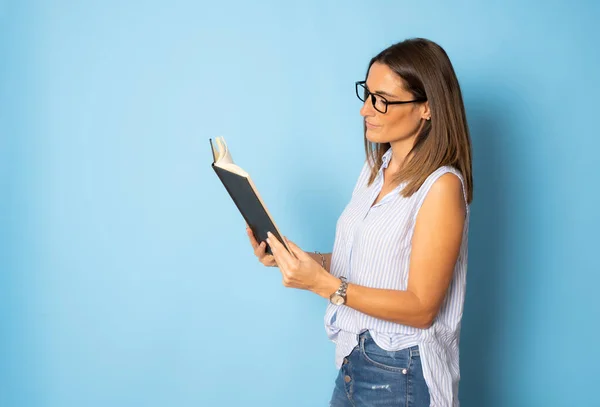 戴眼镜的女人站在蓝色背景下看书 — 图库照片