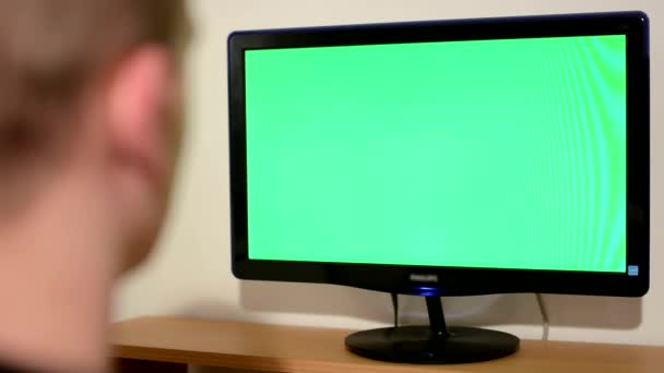 Jonge man kijkt naar de monitor op de tabel in de kamer - groen scherm — Stockvideo