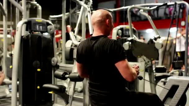 Man versterkt op de machine in het fitnesscentrum, andere atleten op achtergrond. — Stockvideo