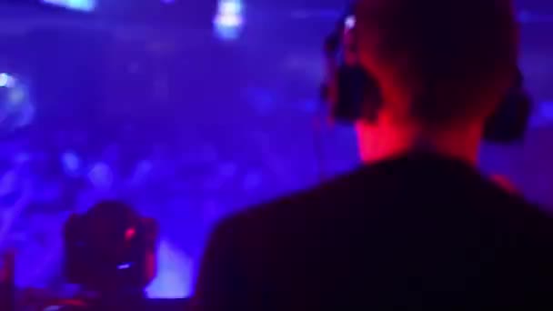 DJ играет на дискотеке, танцует с людьми на заднем плане — стоковое видео