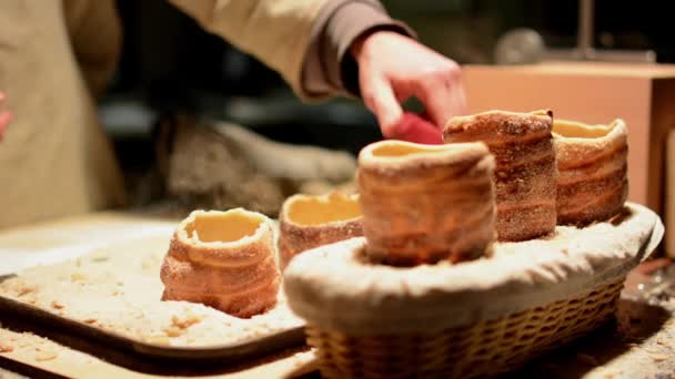 Trdelník (Kamintorte oder Ofenkuchen) im Geschäft (nachts) - Mann im Hintergrund breitet Kuchen mit Haselnusscreme aus — Stockvideo