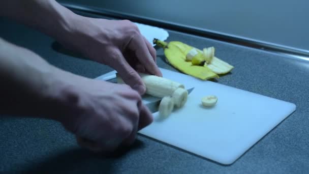 Разрезание банана на ломтики и вставка на тарелку на кухонном столе — стоковое видео