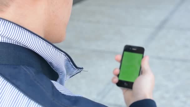 Мужчина смотрит на смартфон, а потом на телефон - зеленый экран — стоковое видео