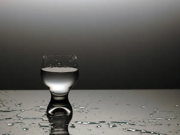 El vaso de agua - el agua derramada Imagen de archivo
