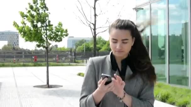 Business woman goes on the street, works on mobile and then phone. Before bussines building — Stock Video