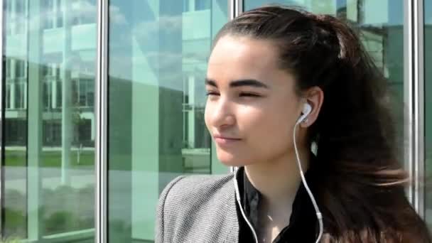 Bussines woman listens to music on headphones before bussines building — Stock Video