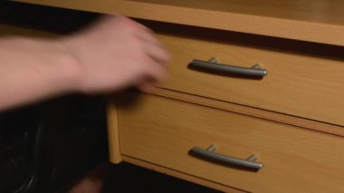 el (genç erkek) bazı kağıtları Masanın çekmecesine alır.