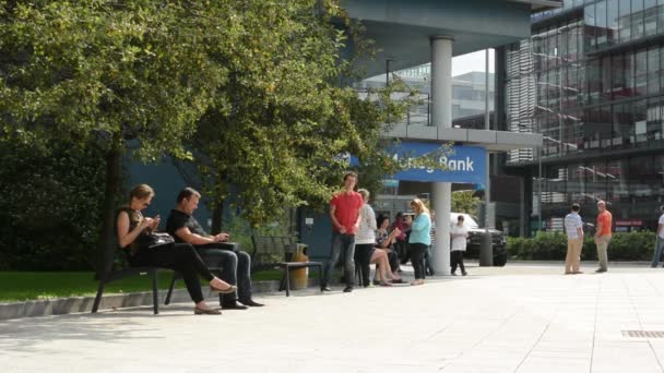 Des gens à l'extérieur du bureau pour une pause cigarette - assis sur un banc et debout — Video