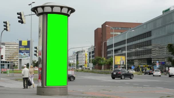 Billboard i byen nær vei - grønn skjerm - bygning, bil og folk i bakgrunnen - gress – stockvideo