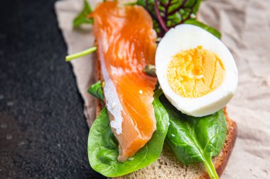 Sandviç somonu smorrebrod yumurtası, yeşil salata karışımı, tahıl ekmekli tost deniz ürünleri açık porsiyon yemek atıştırmalığı masa fotokopisi uzay yiyecek arka planında. 