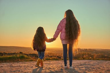 Uçan saçlı iki kız kardeş ufka doğru el ele tutuşuyorlar. ve gün batımını izle. Sonbahar havası kirli bir yoldur. Batan güneşin ışınları, gevşek saçların arasından geçer..