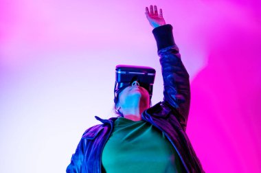 Sanal gerçeklik gözlüklü kadın elini kaldırıyor, renkli ışıklarla aydınlatılıyor..