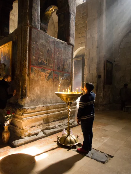 MTSKHETA, GEORGIA - MARCH 10, 2013: Young boy lightens a candle in the Svetitskhoveli Cathedral in Mtskheta. Mtskheta is the old capital of Georgia an it is famous for its cathedral. — Stock Photo, Image