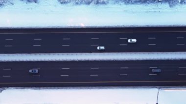 İHA 'nın yol boyunca pürüzsüz uçuşu, otoyol boyunca giden arabalar, kış, ağaçlarda ve yolun kenarında uzanan kar, akşam, gün batımı, güneşten parlayan leylak.