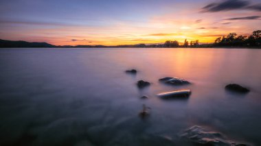 Renkli, güzel bir gün batımı ve suda taşlar.