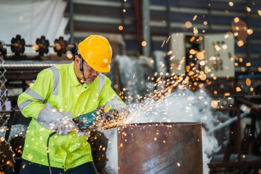 Endüstri işçisi fabrikadaki çelik yapısını öğütmek için elektrikli tekerlek üzerinde çalışıyor..
