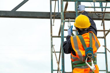 Yükseklik ekipmanında çalışan bir işçi. Güvenlik için kancaları olan işçilerin tutuklanma cihazını seçici odak noktasına getirin. İnşaat arka planındaki işçiler.