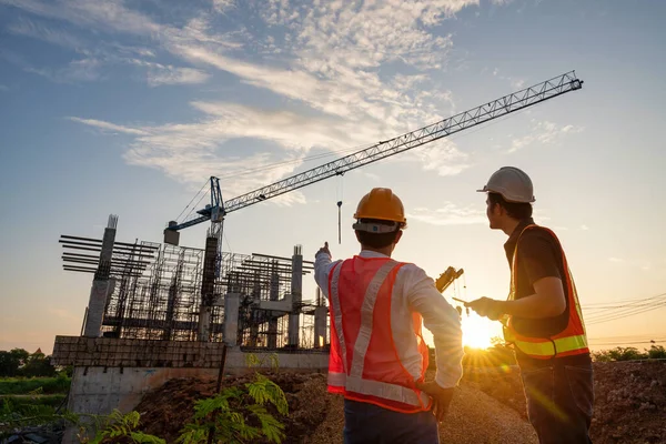 建設プロジェクトの進捗状況とクレーンの背景を監督するアジアの2人の建設エンジニア — ストック写真