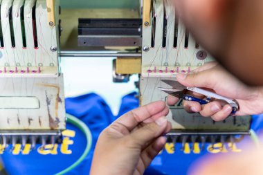 Bir işçi dikiş makinesinde iplik kesmek için makas kullanır. Modern makine ve teknoloji sistemleriyle endüstriyel bölgedeki tekstil fabrikasında nakış.. 