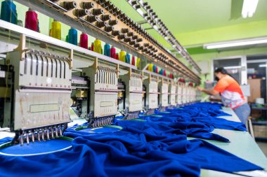 Modern makine ve teknoloji sistemleriyle endüstriyel bölgedeki tekstil fabrikasında nakış makinesiyle çalışan bir işçi. Dikiş makinesinin odak noktasını seç.