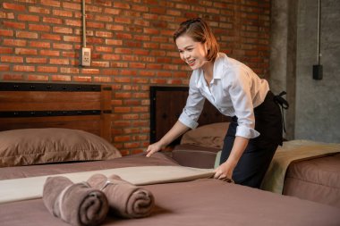 Otel kahverengi tuğla odasında battaniyeyi ayarlayan mutlu genç hizmetçi..