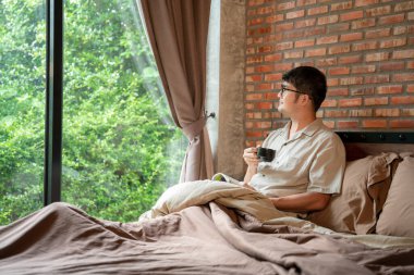 Bir adam sabahları güzel bir gülümseme ile sıcak bir bardak kahve içerken yatak odasında kitap okurken.. 