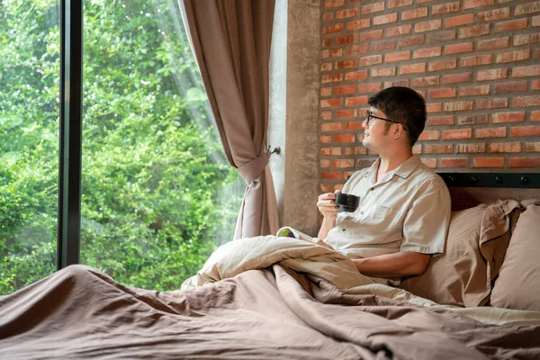 Bir adam sabahları güzel bir gülümseme ile sıcak bir bardak kahve içerken yatak odasında kitap okurken.. 