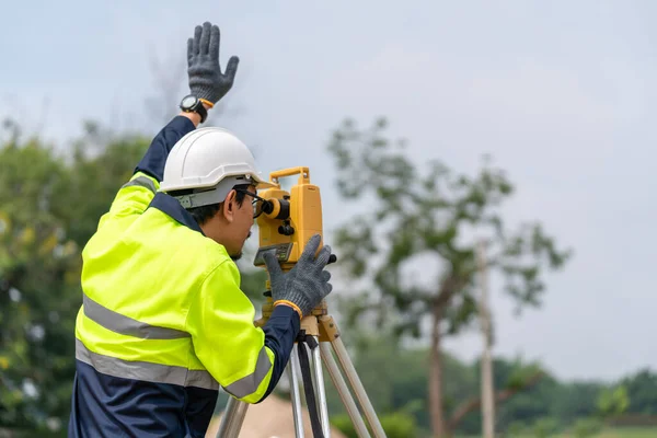 建設現場におけるセオドライト又はトータルポジショニングの作業を行うアジア測量士土木技術者 — ストック写真
