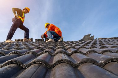 Koruyucu üniformalı profesyonel ve nitelikli çatı ustası, yeni modern bina inşaatının çatısına beton çatı döşemesi yapmak için elektrikli matkap kullanıyor..