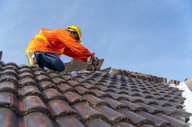 İnşaat alanındaki binanın çatı yapısı üzerinde çalışan bir çatıcı, hava veya pnömatik çivi tabancası kullanan bir çatı ustası ve çatıya beton çatı kiremitleri monte eden bir çatı ustası..