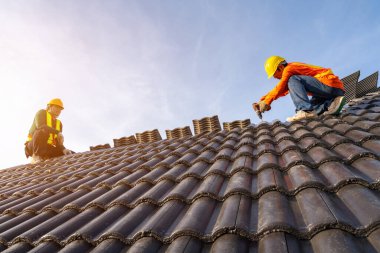 İnşaat alanındaki binanın çatı yapısında çalışan iki Roofer, hava veya pnömatik çivi tabancası kullanan Roofer ve çatıya beton çatı kiremitleri döşeme.