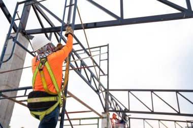 Construction workers are working on steel roof trusses with Fall arrestor device for worker with hooks for safety body harness on the construction site.