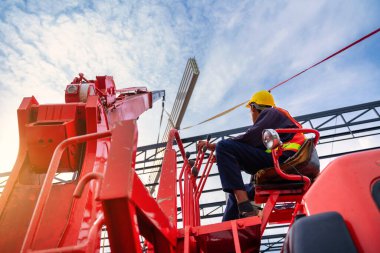 Asian Crane driver, Crane driver sit a top in a mobile crane cabin and working lifting the roof or PU foam roof sheet at the construction site.