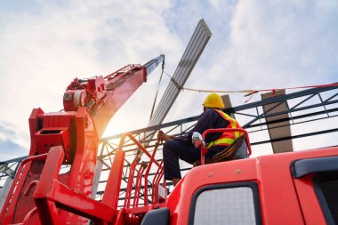A Crane driver sit a top in a mobile crane cabin and working lifting the roof or PU foam roof sheet at the construction site. new roof installation.
