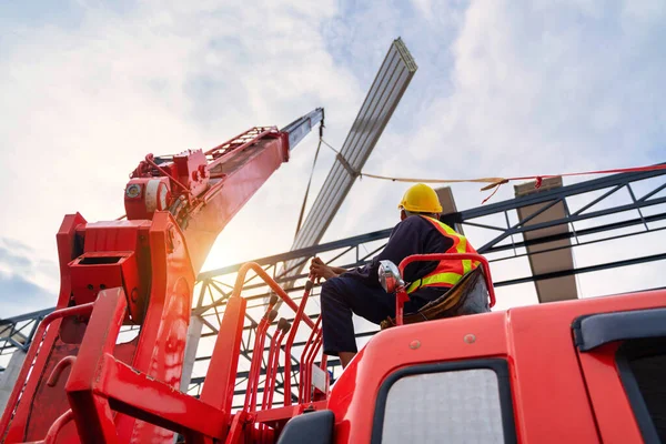 A Crane driver sit a top in a mobile crane cabin and working lifting the roof or PU foam roof sheet at the construction site. new roof installation.