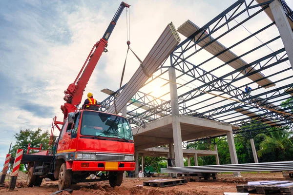 Crane driver is working on the mobile crane and lifting the roof or the PU foam roof sheet at the construction site. Install a new roof.