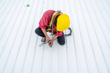 A Roofer worker using electric drill nail gun and installing PU foam roof sheet on top of the new roof, Concept of residential building under construction.