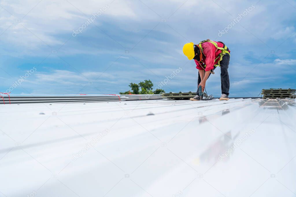 A Construction worker install new roof, Electric drill used on new roofs with white Metal Sheet. Roofing tools, Safety body construction, Working at height equipment. building