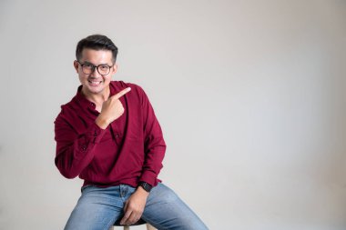 Asyalı adam parmaklarıyla stüdyonun gri arka planını işaret ederek gülümsüyor. Yakışıklı, sağlıklı bir genç adam. Malların fiyatını düşürmek için satış ve tanıtım kavramları.