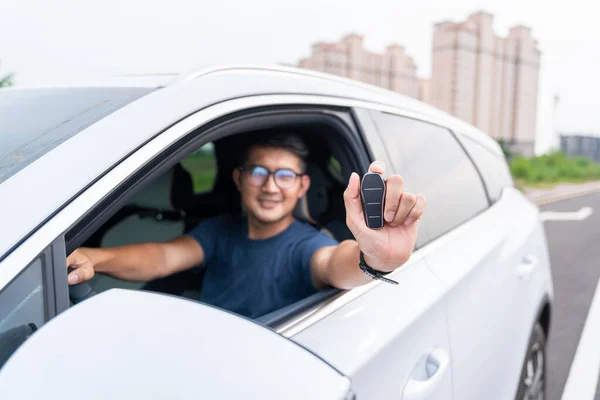 Asian man showing a car key inside his new electric vehicle. Electric car. EV Car. EV vehicle.