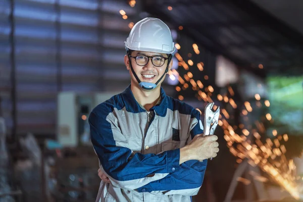 亚洲工程师微笑着年轻的男性管道工 身穿安全制服 头戴硬礼帽 身穿管扳手交叉立臂 在工厂里使用平板止回钢或金属制造工艺 — 图库照片