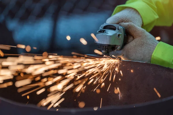 Close Up hand of Industrial Worker Using Angle Grinder and Cutting a Metal Tube. Worker in Safety Uniform and Hard Hat Manufacturing Metal Structures. Heavy Industry.