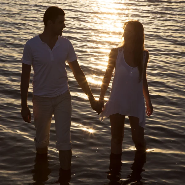 Pariskunta kävelee meren rannalla auringonlaskun aikaan — kuvapankkivalokuva