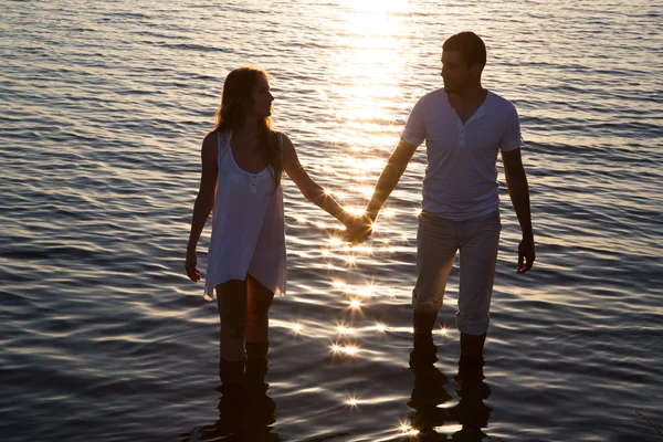 Casal caminhando pelo mar ao pôr do sol — Fotografia de Stock