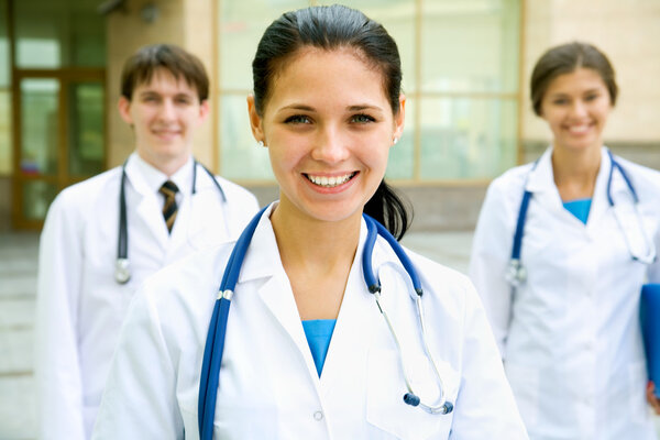 Jeunes médecins debout devant l'hôpital et regardant la caméra — Image Jeunes médecins — Photo