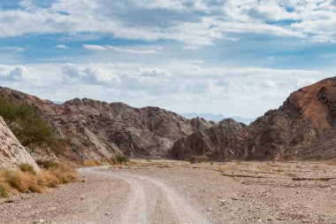 Rural gravel road turns in rocky desert between hills, sandy hills 