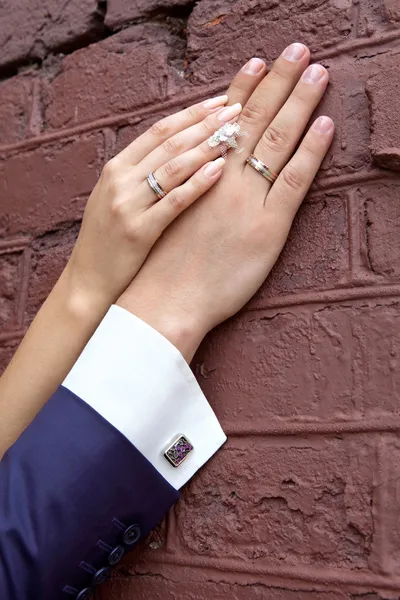 Bröllop. brudens hand vilar på brudgummens hand. bara gifta par händer tillsammans. familjen parets händer med ringar och en cuffling bredvid tegelvägg. — Stockfoto
