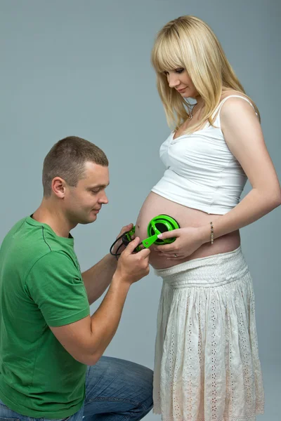 Baby buik luisteren naar muziek. man ter zwangere vrouw buik, de baby luisteren naar muziek de hoofdtelefoon. — Stockfoto