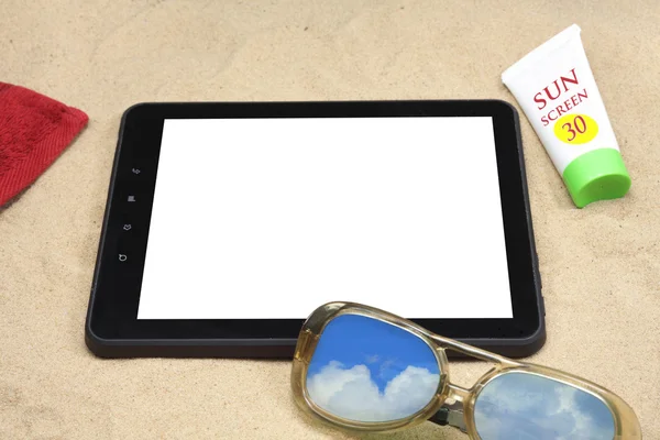 Summer background with digital tablet, sunglasses, sun cream and a towel on the sand.