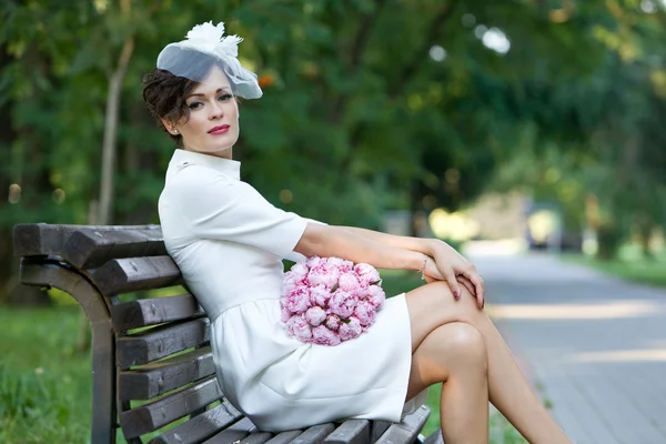 Düğün. bir buket çiçek ile bir bankta oturan bir şapka peçe ile şık kılıf içinde güzel bir gelin elbise. — Stok fotoğraf